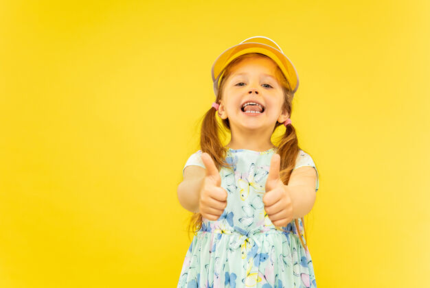 长美丽动情的小女孩被隔离在黄色背景上半幅快乐的孩子的肖像 穿着裙子 戴着橘黄色的帽子 表现出一种ok的姿态夏天的概念 人类的情感 童年欢呼脸年轻