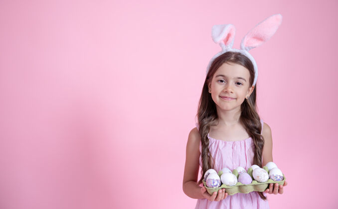 节日快乐的小女孩 有复活节兔子的耳朵 手里拿着一盘鸡蛋放在粉红色的墙上复活节的概念兔子女孩兔子