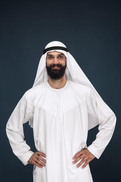 微笑深蓝色工作室背景上的半身阿拉伯沙特商人肖像年轻男模站着微笑商业 金融 面部表情 人类情感的概念反应阿拉伯语手势