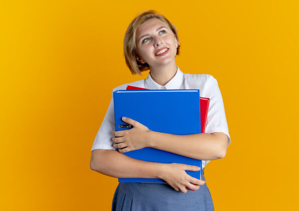 俄罗斯年轻的笑容可掬的金发俄罗斯女孩拿着文件夹 在橙色背景上孤立地向上看 还有一个复制空间文件微笑金发