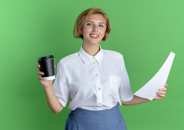 年轻年轻的微笑的金发俄罗斯女孩拿着咖啡杯和纸被隔离在绿色背景与复制空间杯子咖啡床单