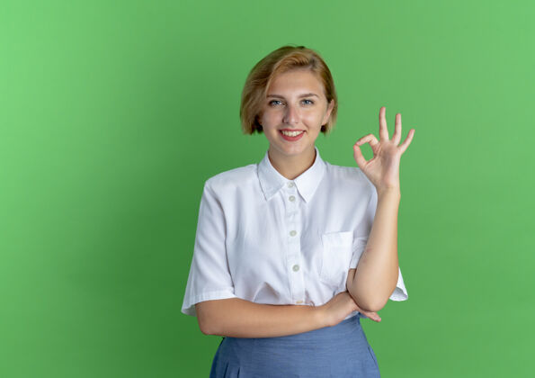 手势年轻微笑的金发俄罗斯女孩手势ok手势 绿色背景上有复制空间手好年轻