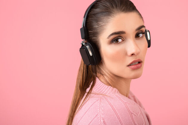 女士穿着粉色毛衣戴着无线耳机听音乐的年轻漂亮女人无线立体声模特