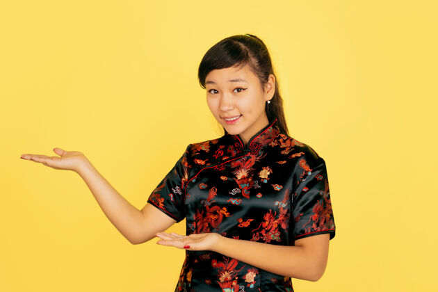 亚洲微笑可爱 展现在身边2020年中国新年快乐黄色背景上的亚洲少女肖像身着传统服装的女模特看起来很快乐庆祝 人类情感复制空间火花手旗袍