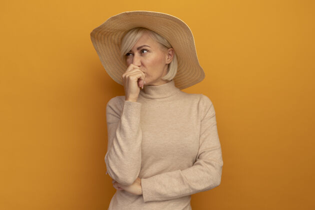 人一个戴着沙滩帽 金发碧眼的斯拉夫女人把手放在橘色墙壁上的嘴巴前面帽子人站