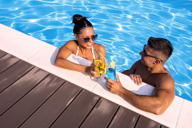 漂亮在游泳池里 一群微笑的夫妇拿着鸡尾酒的高角度镜头海滩水休闲