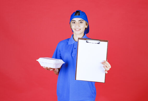 工人身穿蓝色制服的女快递员拿着一个白色的外卖箱 出示清单供签字送货成人人类
