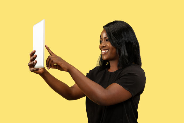 女商人年轻的非洲裔美国女性 隔离在黄色的工作室背景下 面部表情美丽的女性肖像人类情感的概念 面部表情使用平板电脑进行自拍或视频录像机魅力情感美国人