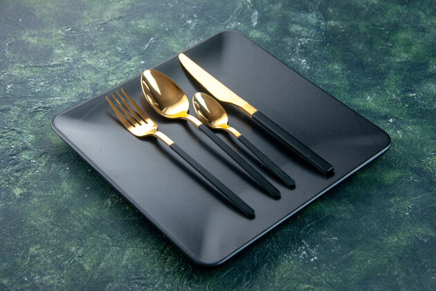 叉子正面图黑色的盘子和金色的勺子刀叉在黑暗的背景上刀厨房笔记本