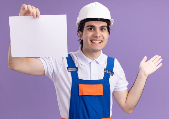 空白身穿施工制服 头戴安全帽的年轻建筑工人站在紫色的墙上 面带微笑地看着前面的空白页男人年轻建筑工