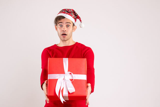 人前视图：戴着圣诞帽的年轻人拿着他的礼物 背景是白色的前面帽子冬天