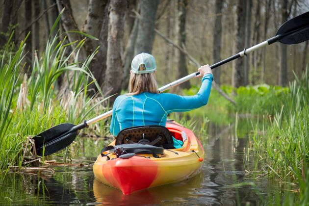 女性特写镜头：一个女孩在白天阳光下 在一条绿树环绕的小河上划独木舟船皮划艇人