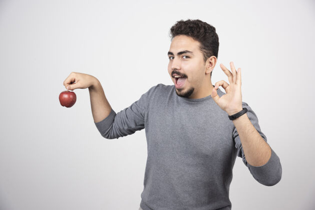 男孩一个黑发男人拿着一个红苹果站在灰色的树上举行模型水果