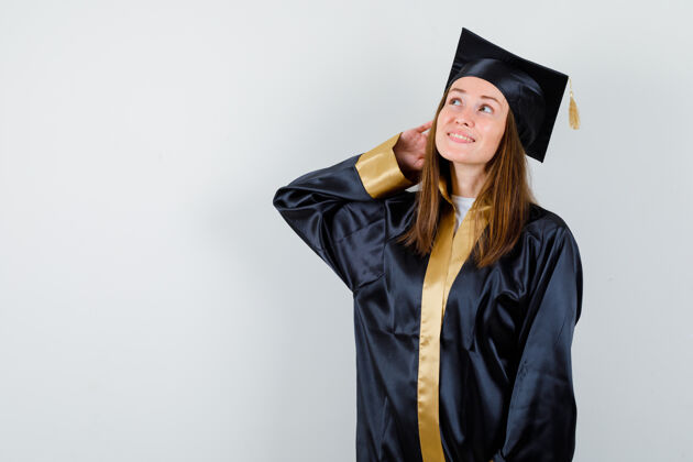 年轻女毕业生的肖像摆姿势 同时在学术服装和期待充满希望的正面视图仰望骄傲学校长袍