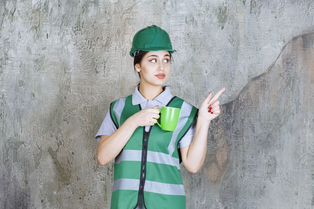 雇员戴绿色头盔的女工程师拿着一个绿色的咖啡杯职员女人休息