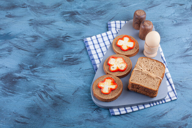 茶毛巾煮鸡蛋和切片面包放在茶巾板上 放在蓝色的桌子上美味美味酵母