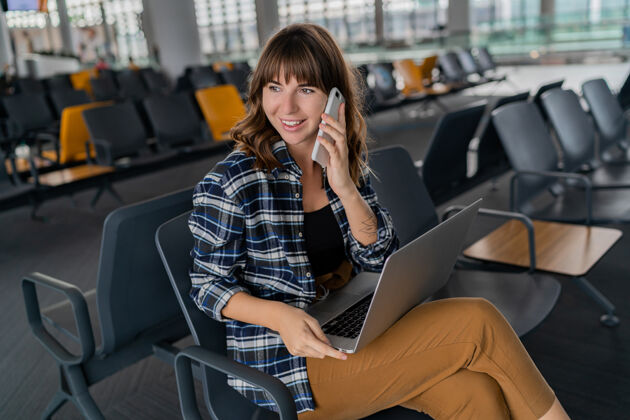 电脑机场年轻女乘客带着智能手机和笔记本电脑坐在候机大厅等待航班假日室内美丽