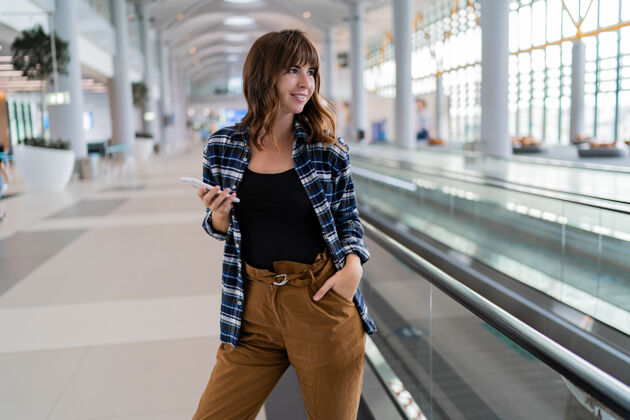 学生女性用智能手机穿过机场终端女性等待