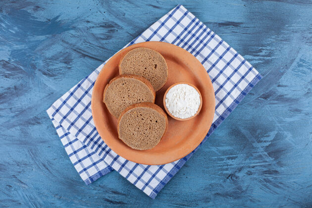 酵母把切片的面包和一碗面粉放在茶巾的盘子里 放在蓝色的桌子上糕点美味茶巾
