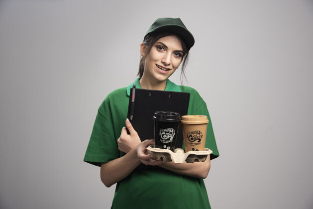 帽子穿着绿色制服的女送货员拿着剪贴板和咖啡杯工人女快递