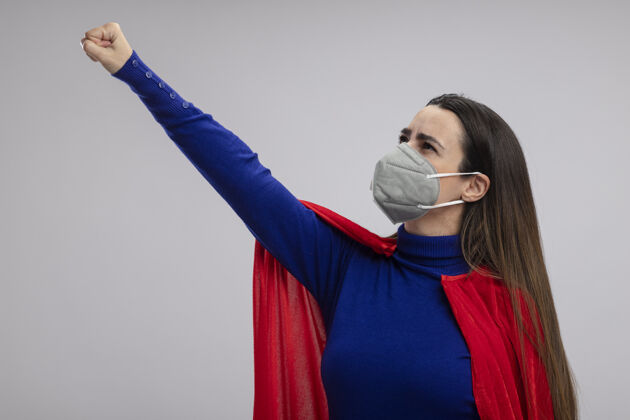 举起来年轻的超级英雄女孩戴着医用面具举起拳头隔离在白色背景上超级英雄面具女孩