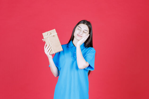 女人穿着蓝色衬衫的女人手里拿着一个纸板小礼盒 看起来又困又累疲惫姿势庆祝