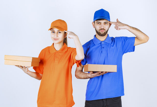 服装穿着蓝黄制服的快递员男孩和女孩拿着纸板外卖盒和购物包 看上去很困惑 在思考新的想法工人员工年轻人