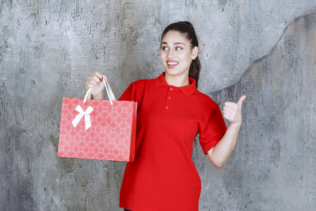 人一个穿着红衫的年轻女子手里拿着一个红色的购物袋 手上显示着积极的手势成人包享受