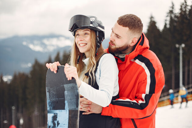 运动穿着滑雪板套装的情侣在山上运动的人手里拿着滑雪板在地平线上运动的概念站立寒冷两个