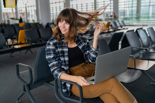 飞机年轻的女乘客拿着笔记本电脑坐在候机大厅等待航班在线旅游者预订