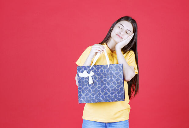 梦幻一个穿着黄色衬衫的女人手里拿着一个蓝色的购物袋 看起来又累又困人时尚女性