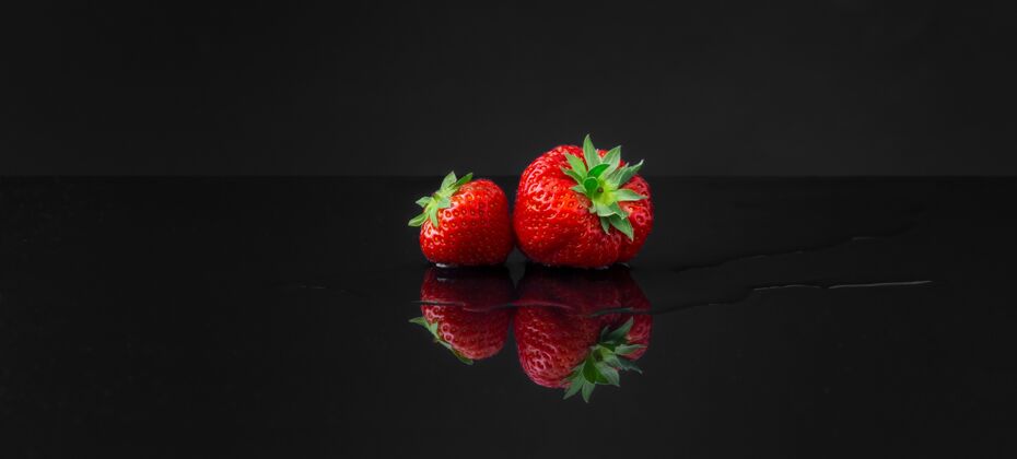 水平在黑色反射面上水平广角拍摄两个红色草莓新鲜角度葡萄干