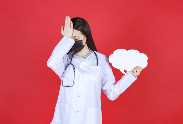 医学女医生戴着听诊器 戴着黑色口罩 手拿着一张云状的空白问讯台和头治疗装备疾病