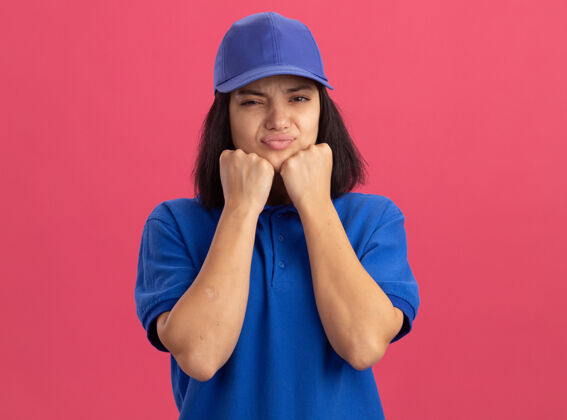失望穿着蓝色制服 戴着帽子的年轻送货员站在粉色的墙上 歪歪着嘴 带着失望的表情立场年轻表情