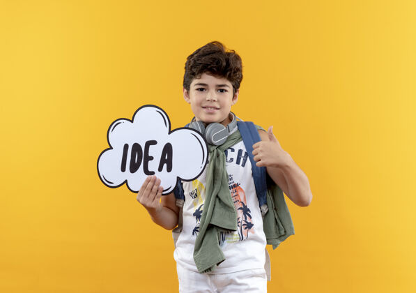 男孩高兴的小男孩戴着背包和耳机拿着创意泡泡他的大拇指孤立的黄色背景包学校创意