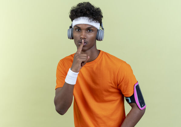 相机看着镜头年轻的美国黑人运动男子戴着头带和腕带和电话臂带耳机显示沉默的姿态隔离在绿色背景穿着乐队头带