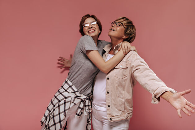 女士正面两个短发女人戴着现代眼镜 穿着时尚的浅色衣服 在粉色背景下拥抱微笑短发老年粉色