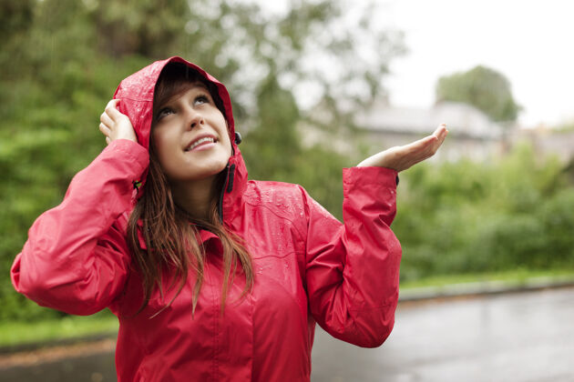 湿穿着雨衣的美女在检查雨水下雨散步站