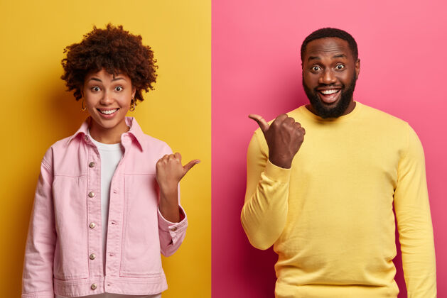 肖像积极的非裔美国女人和男人互相指指点点 笑容满面 神情热情 穿着休闲服 隔离在粉黄色的墙上 心情愉快 关系友好休闲满意成人