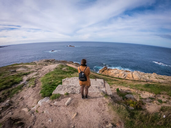 时尚高角度拍摄了一位时尚女性站在西班牙科鲁纳附近平静的海面上观看海岩石年轻