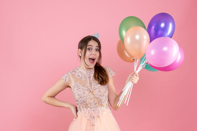 气球前视图兴高采烈的派对女孩 戴着派对帽 手里拿着气球粉色手派对