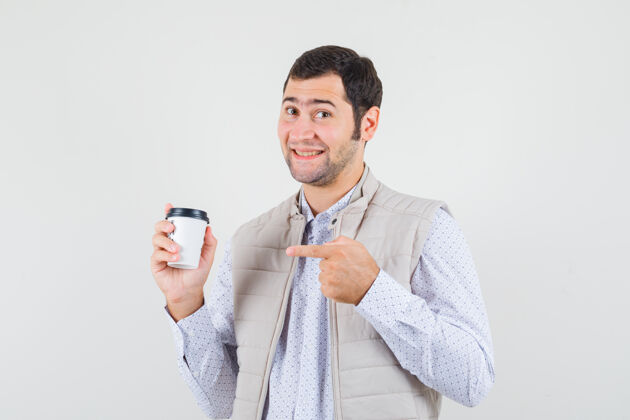 人身穿米色夹克的年轻人用食指指着外卖咖啡杯 神情乐观 正面看去前面年轻人商人