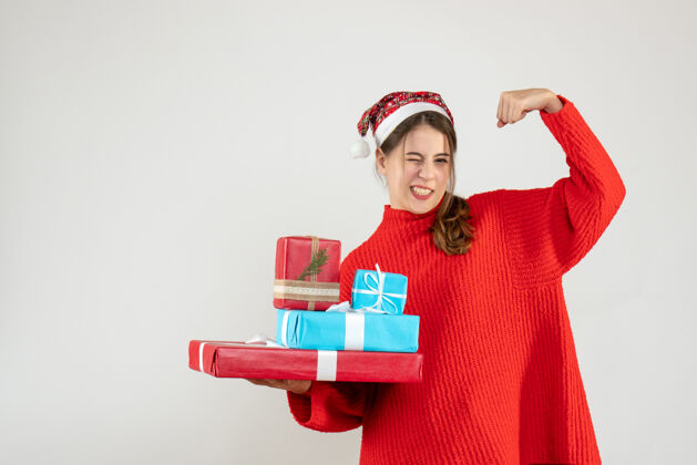 肌肉前视图兴高采烈的女孩 戴着圣诞礼物的圣诞帽 展示着她的肌肉快乐圣诞节欢乐