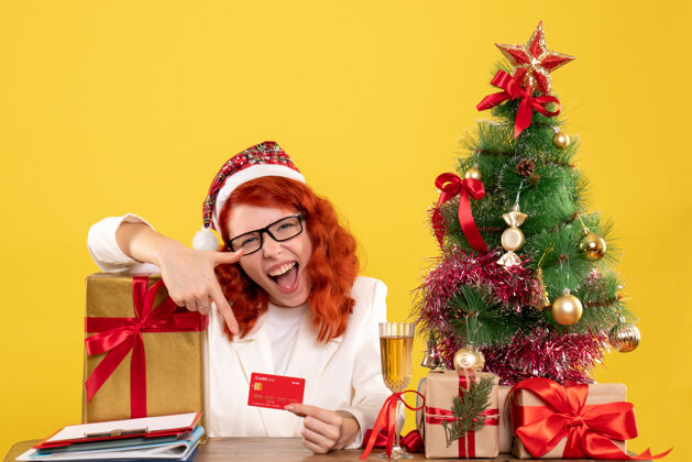 成人前视图女医生拿着银行卡在圣诞礼物和圣诞树周围人庆祝礼物
