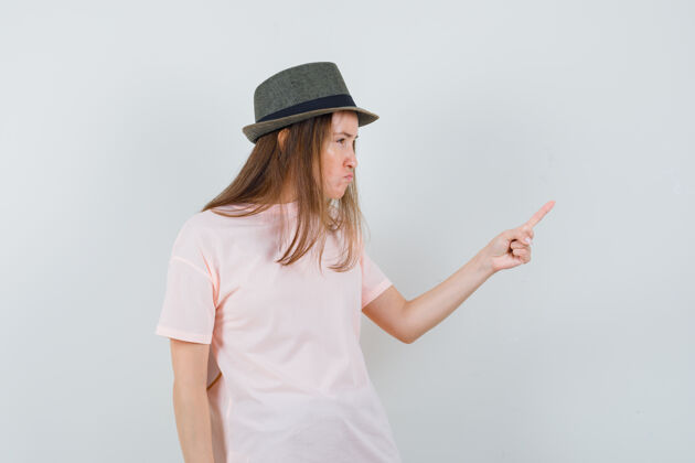 女性一位戴着粉色t恤帽子的年轻女士用手指警告 看起来很恶毒黑发优雅兴奋