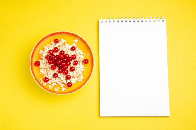 艺术顶视图浆果红色浆果燕麦片在橙色碗白色笔记本酸水果笔记本