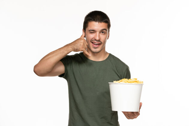 土豆正面图身穿绿色t恤的年轻男子拿着篮子和土豆在白色的墙上孤独地享受电影杯子电影肖像