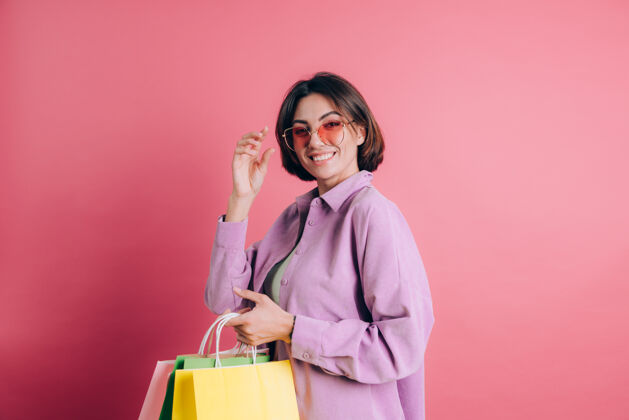微笑背景上穿着休闲毛衣的女人拿着五颜六色的包戴着夏日太阳镜快乐地购物人时尚销售