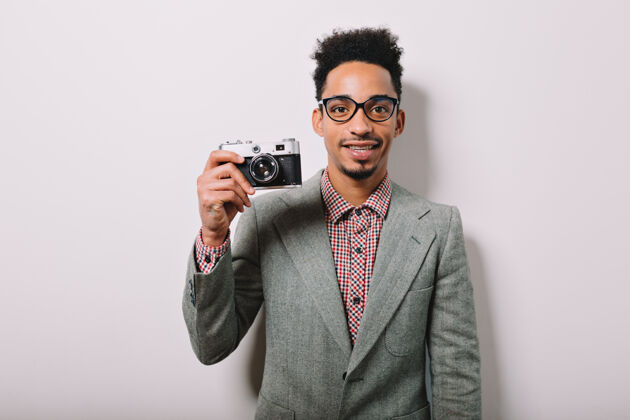 积极非洲男人的画像戴着眼镜和灰色夹克 灰色上有复古相机非洲欢呼自信