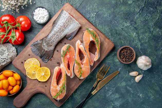 深色上图：生鱼片柠檬片青椒木砧板西红柿餐具放在深色的桌子上生鱼切片剪刀